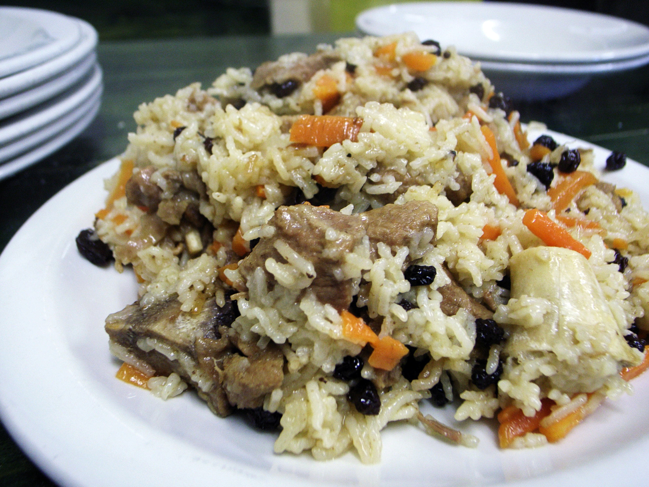 A plated qabuli palau, long-grain rice topped with carrot julienne and raisins, served with lamb